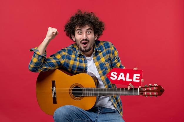 Front view young male sitting with guitar on red wall concert live musician play music color applause