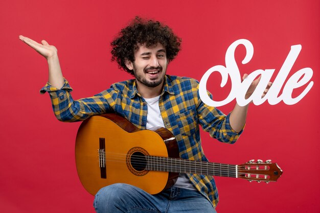 Front view young male sitting with guitar on red wall music applause live musician color sale