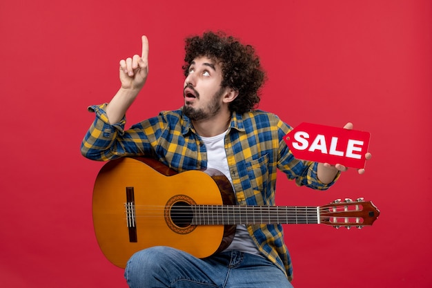 赤い壁にギターを持って座っている正面図若い男性音楽色拍手ライブミュージシャンセールプレイ