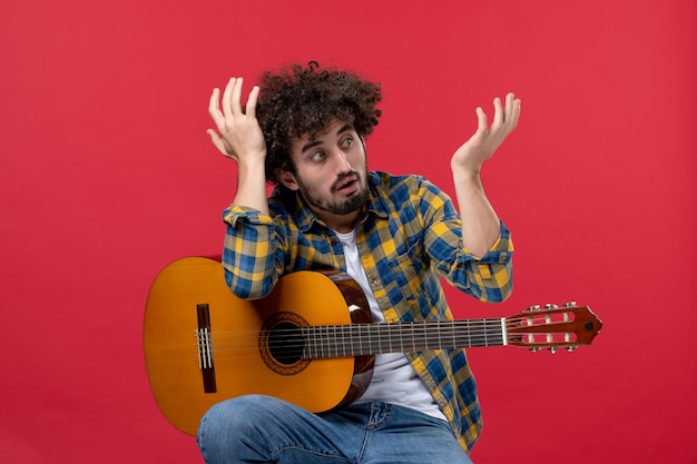 Foto gratuita vista frontale giovane maschio seduto con la chitarra sulla parete rossa musica musicista colore applauso concerto dal vivo
