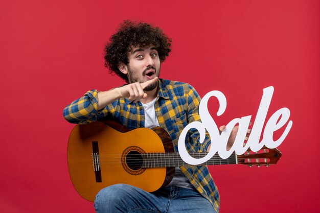 Вид спереди молодой мужчина сидит с гитарой на красной стене, играет на концерте, распродажа музыкантов, цветных аплодисментов вживую
