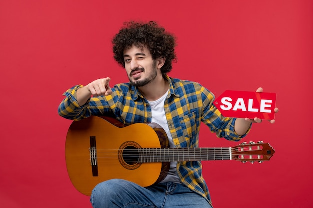빨간 벽에 기타와 함께 앉아 있는 전면 보기 젊은 남성 연주 음악 공연 음악가 라이브 콘서트 판매 박수