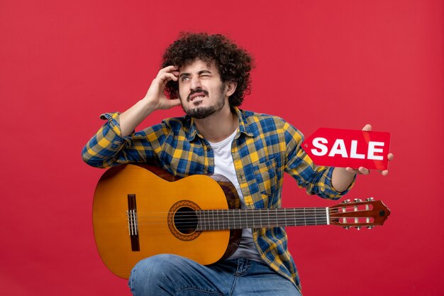 Front view young male sitting with guitar on red wall play music performance musician color applause live sale