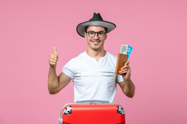 ピンクの壁の航海旅行飛行機の男性の写真の色の休暇で飛行機のチケットを笑顔で保持している若い男性の正面図