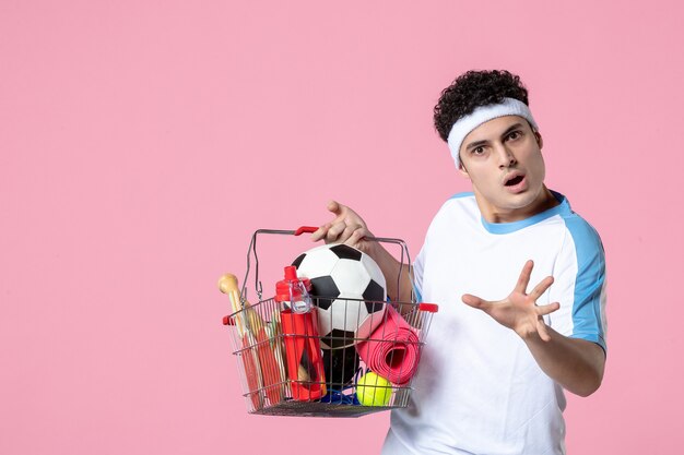 Front view young male in sport clothes with basket full of sport things pink wall