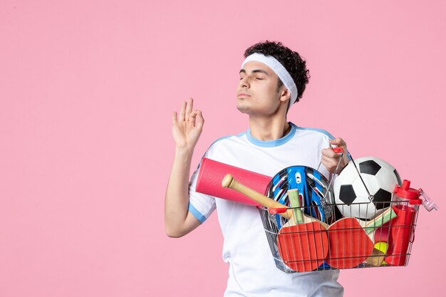 Front view young male in sport clothes with basket full of sport things pink wall