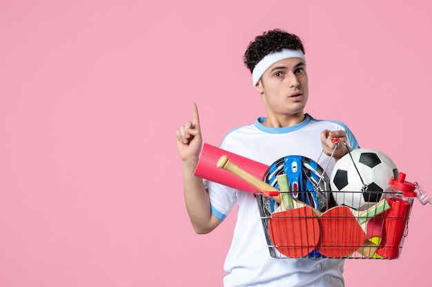 Free photo front view young male in sport clothes with basket full of sport things pink wall