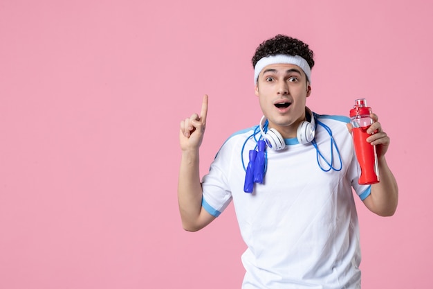 Front view young male in sport clothes with skipping rope and water pink wall