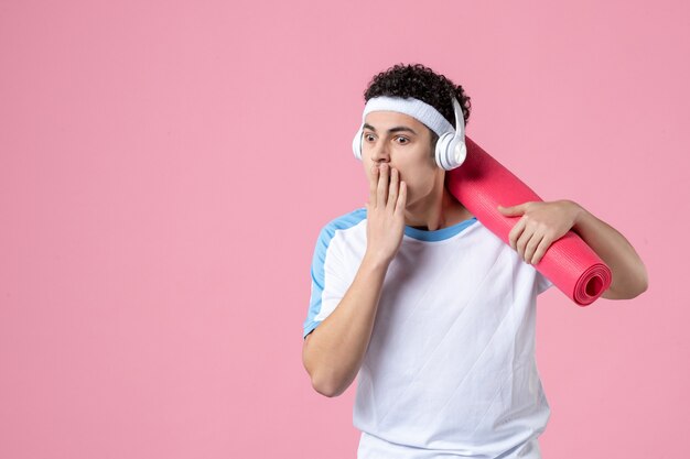 Front view young male in sport clothes with yoga mat and headphones on pink wall