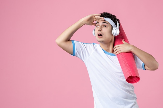 Foto gratuita giovane maschio di vista frontale in vestiti di sport con la stuoia di yoga che esamina la distanza sulla parete rosa