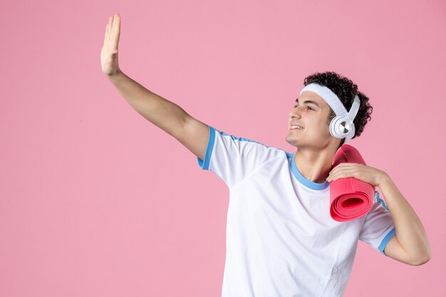 Вид спереди молодой мужчина в спортивной одежде с ковриком для йоги на розовой стене