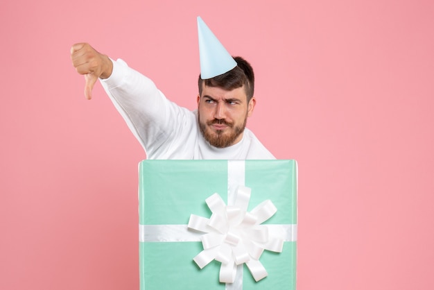Вид спереди молодой мужчина, стоящий внутри подарочной коробки на розовой рождественской фотографии, цветная эмоция, пижамная вечеринка
