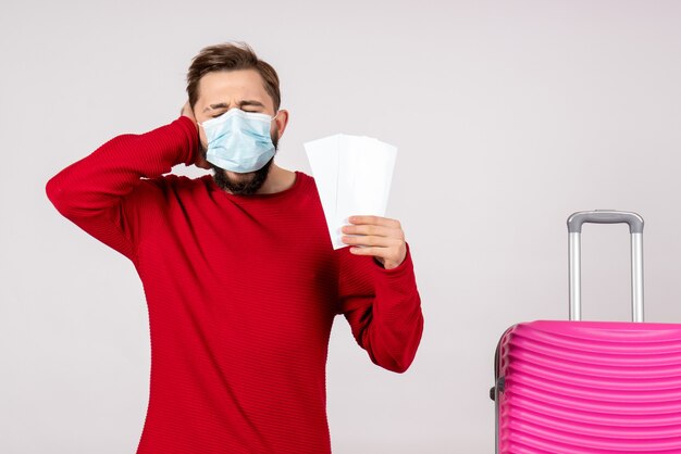 Foto gratuita giovane maschio di vista frontale nella maschera sterile che tiene i biglietti sul viaggio di colore del virus di emozione di vacanza di covid-aereo della parete bianca