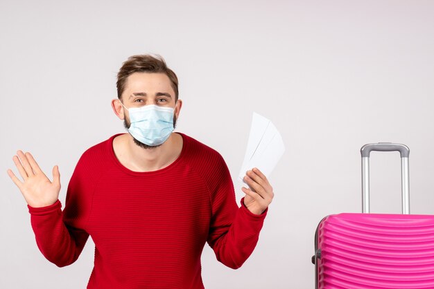 Front view young male in sterile mask holding tickets on white wall covid- plane vacation emotion virus flight trip