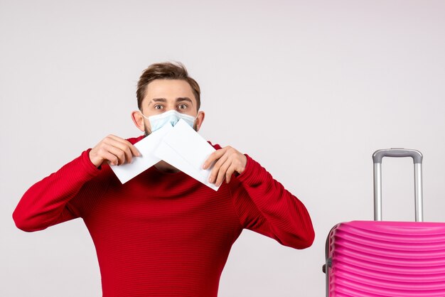 Front view young male in sterile mask holding tickets on white wall covid- plane vacation virus flight color trip