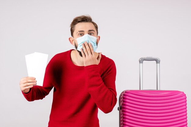 白い壁の航海covid-飛行旅行休暇ウイルス色の感情のチケットを保持している滅菌マスクの正面図若い男性