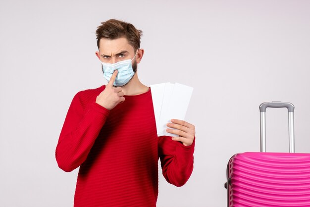 Front view young male in sterile mask holding tickets on white wall voyage covid- trip vacation color emotion flight