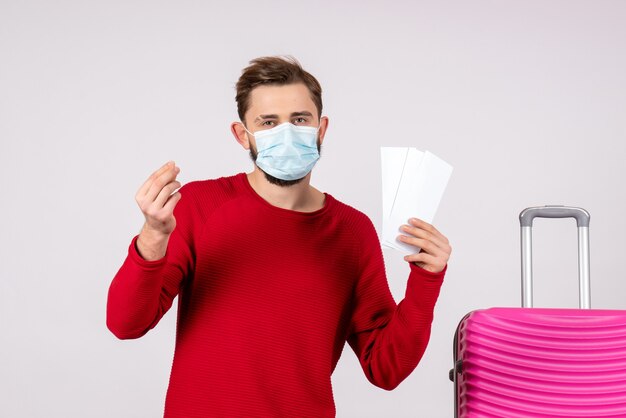 白い壁の航海covid-旅行休暇色感情ウイルス飛行のチケットを保持している滅菌マスクの正面図若い男性