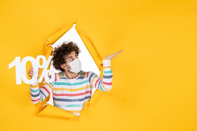 Free photo front view young male in sterile mask holding writing on yellow photo health coronavirus pandemic sale