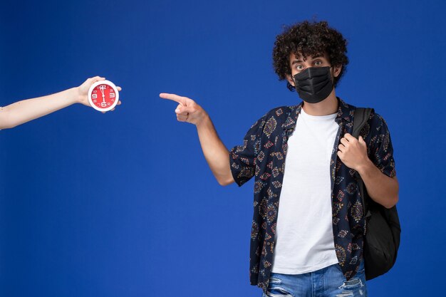 Front view young male student wearing black mask with backpack on light-blue background.