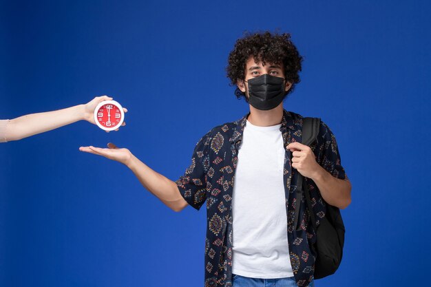 Front view young male student wearing black mask with backpack on light blue background.