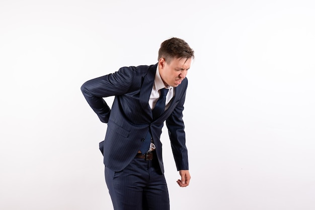 Front view young male suffering from back ache in classic strict suit on white background