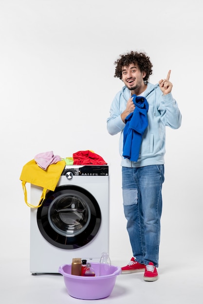 Front view of young male taking out clean clothes from washer on white wall