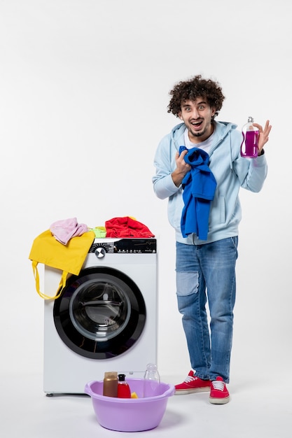白い壁の洗濯機からきれいな服を取り出している若い男性の正面図