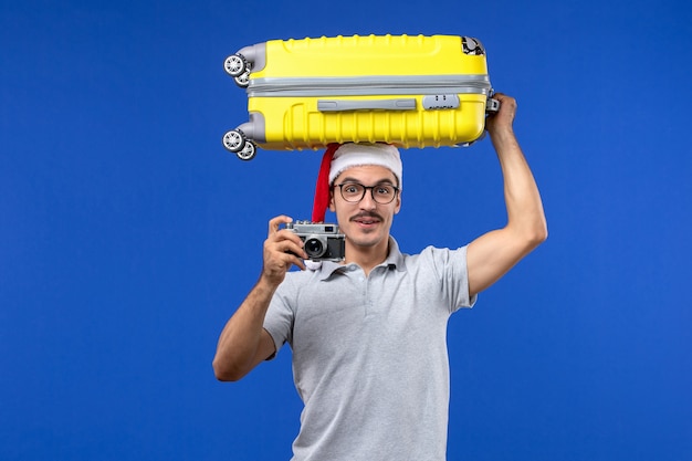 Front view young male taking photo and holding bag on blue wall flights vacation plane