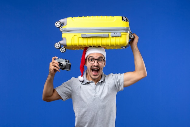 Front view young male taking photo and holding bag on blue wall flights vacation planes