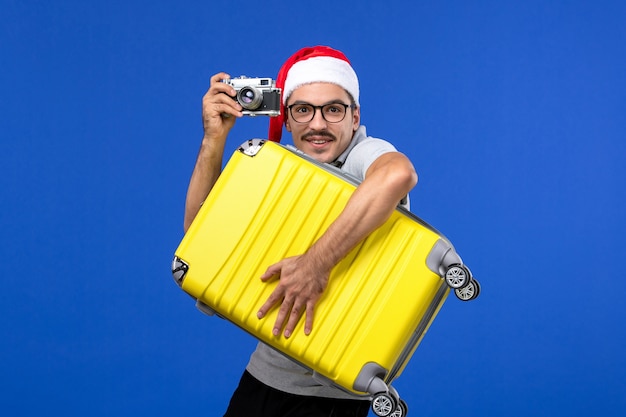 Giovane maschio di vista frontale che cattura foto con la macchina fotografica sugli aerei di vacanza di volo della parete blu