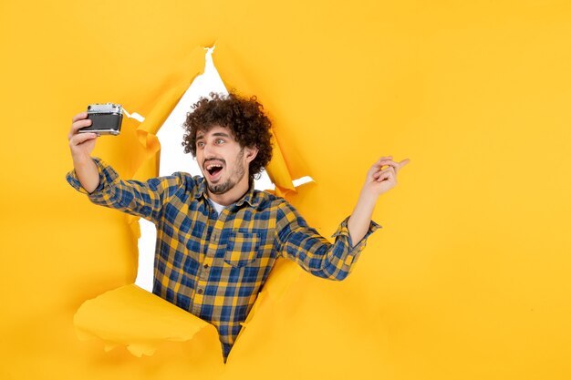 Вид спереди молодой мужчина, делающий фото с камерой на желтом фоне