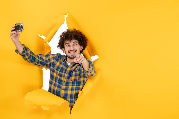 Front view young male taking photo with camera on yellow background