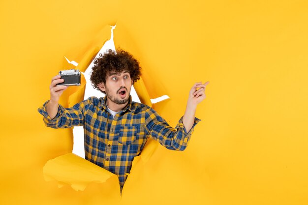 Front view young male taking photo with camera on yellow background