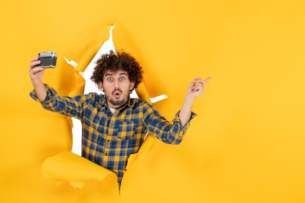 Front view young male taking photo with camera on yellow background