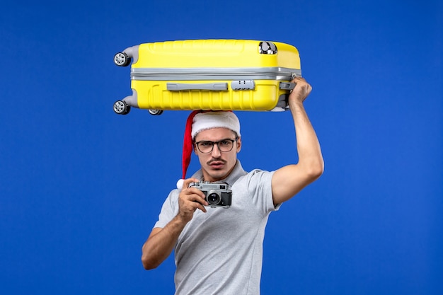 Giovane maschio di vista frontale che cattura le foto e che tiene la borsa sulla vacanza di volo dell'aereo della parete blu