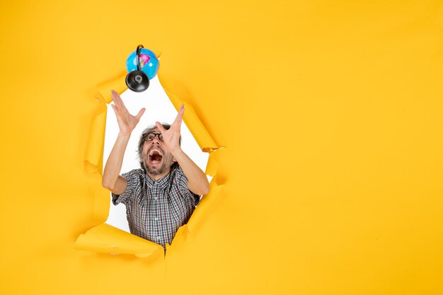 Front view of young male throwing and catching earth globe on yellow wall