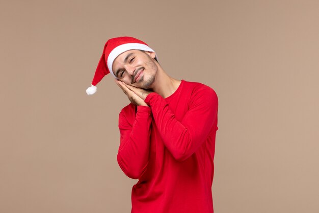 疲れて茶色の背景の感情のクリスマス休暇で眠ろうとしている若い男性の正面図
