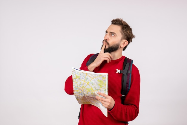Front view young male tourist with backpack exploring map thinking on white wall plane city vacation emotion human color tourism