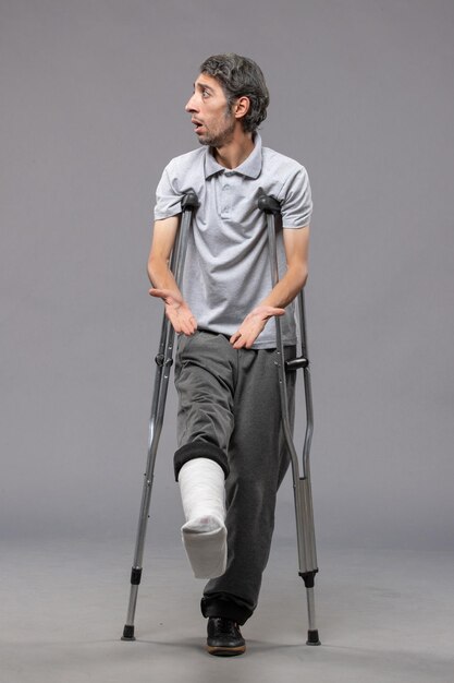 Front view young male using crutches due to broken foot on grey desk pain foot disable leg broken accident