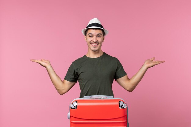 Вид спереди молодого мужчины в отпуске с большой сумкой и улыбкой на розовом пространстве