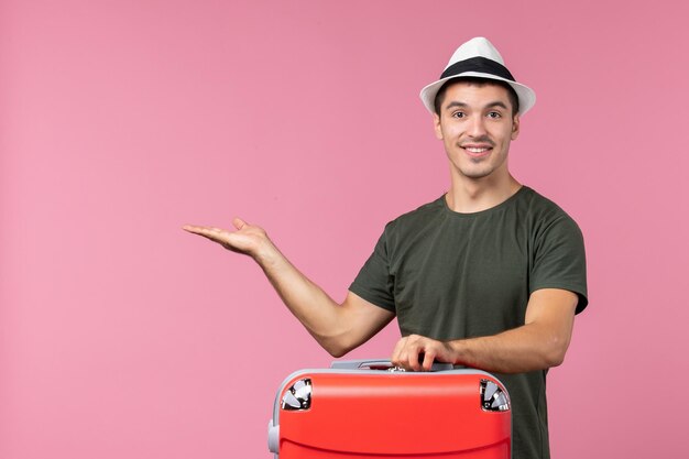Вид спереди молодой самец в отпуске со своей красной сумкой на розовом полу, путешествие по морю, путешествие, человек, путешествие, отпуск