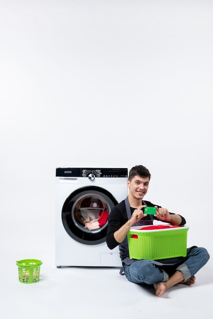 Front view of young male waiting until the end of clothes washing on a white wall