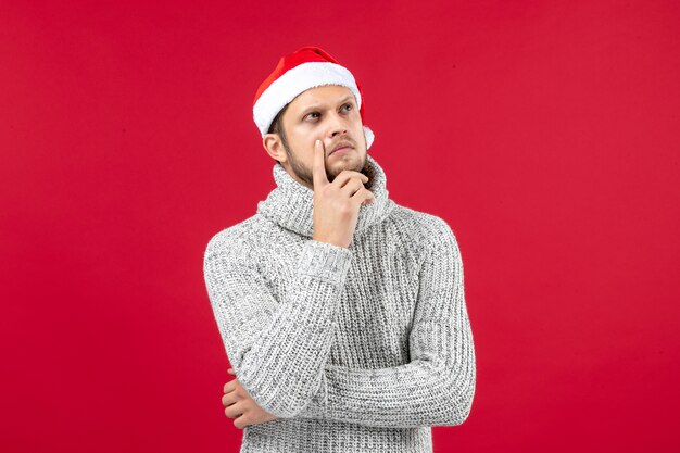 Front view young male in warm jersey with holiday cap thinking on red background