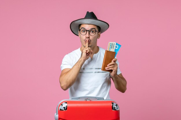 ピンクの壁の航海旅行飛行機の男性の写真の色の休暇で帽子をかぶって飛行機のチケットを保持している正面図若い男性