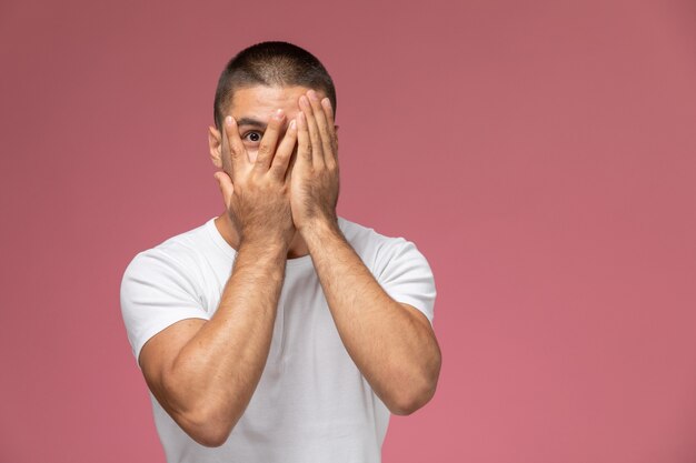 Front view young male in white shirt covering his face on pink background