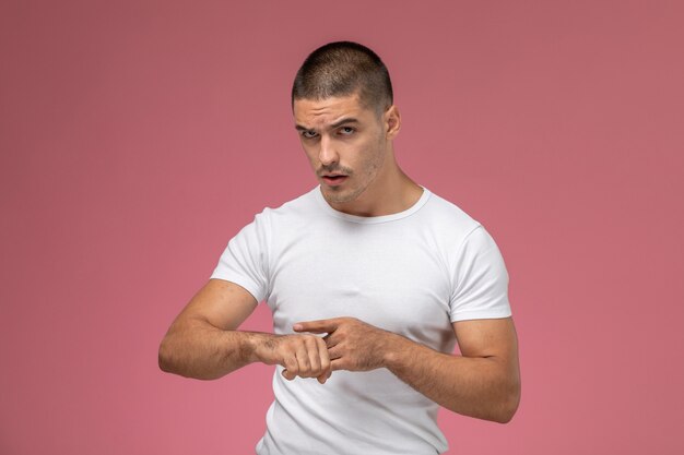 Front view young male in white shirt pointing out at his wrist on pink background