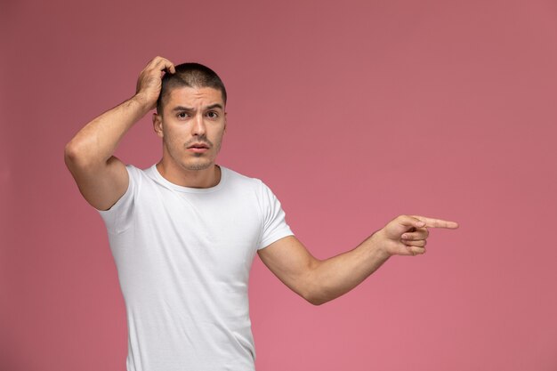 Front view young male in white shirt posing with hesitating expression on pink background