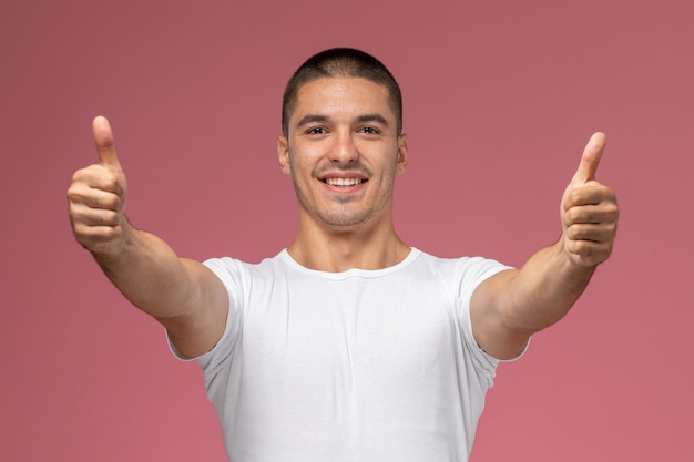 Front view young male in white shirt showing like signs smiling on pink background 