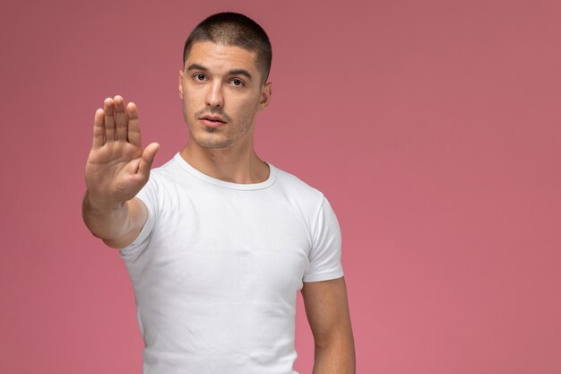 Front view young male in white shirt showing stop sign on pink background 